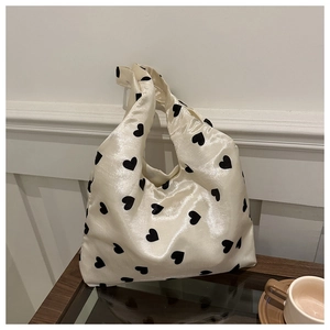 Detailed view of a cream satin knot handbag with black heart prints on a wooden table