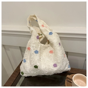 Detail of a beige knitted tote bag featuring colorful flower embroidery and fringe texture