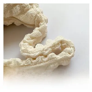 Gros plan sur la bandoulière blanc cassé à texture bulle d'un sac plissé souple