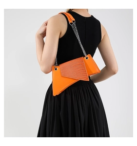 Close-up of bright orange crocodile texture bag with metal chain on a black dress