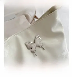 Gros plan du sac seau blanc crème avec un ornement papillon en métal argenté poli