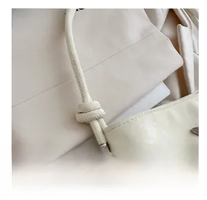 Détail du sac seau en cuir crème avec bandoulière nouée et embouts en métal argenté