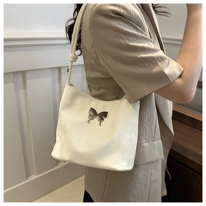 Gros plan du sac à bandoulière ivoire avec papillon en métal argenté et texture suédée