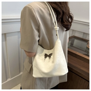 Détail d'un sac à épaule en velours blanc avec logo papillon argenté et bandoulière nouée