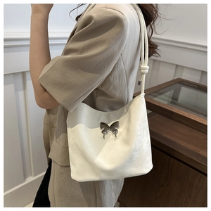 Sac à bandoulière ivoire avec détail papillon en métal porté sur l'épaule de la femme
