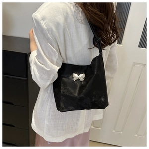 Détail du sac à bandoulière noir avec emblème papillon argenté et finition satinée