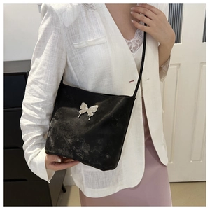 Détail d'un sac à bandoulière noir avec papillon argenté porté par un mannequin