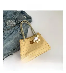 Detail of beige checkered tote bag with rope handles and soft white pom-pom charm