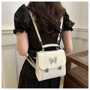 Back view of a mini butterfly backpack in cream faux leather worn by a female model