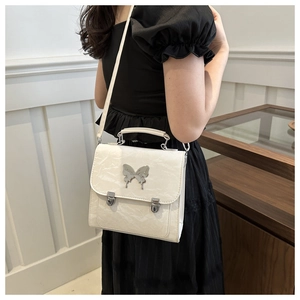 Detail of cream pleated mini bag with a large silver butterfly buckle shown by a model