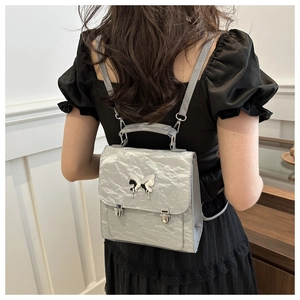 Detail of silver pleated mini backpack featuring a metallic butterfly emblem and buckle straps