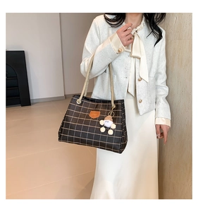 Detail of black checkered tote bag featuring a leather logo and woven shoulder strap