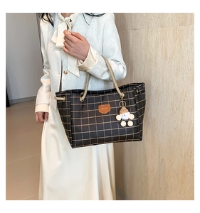 Close-up of black plaid leather tote with woven handles and a cute plush doll pendant