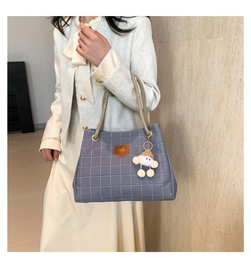Detail of grey-blue checkered tote bag with woven rope handles and plush charm pendant