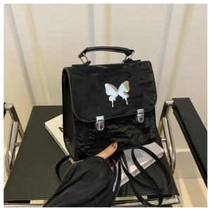 Close-up of a mini black butterfly backpack with shiny wrinkled texture and metal buckle
