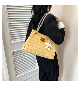 Detailed view of yellow plaid canvas tote with leather logo and plush bear charm