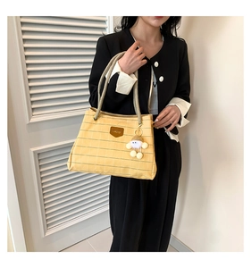 Detail of yellow checkered tote bag with woven handles and white plush doll charm