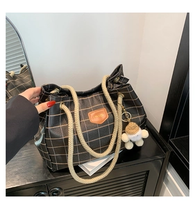 Detail of black tote bag with gold grid pattern, rope handle and plush bear charm