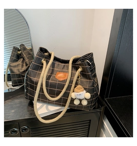 Detail of black plaid tote bag featuring thick rope handles and a cute plush doll charm