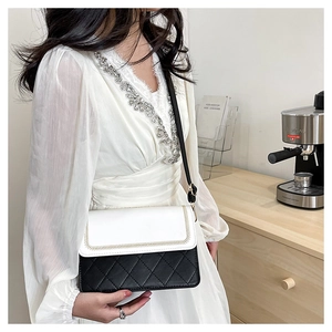 Detail of a black and white quilted crossbody bag with gold stitching on model in home setting