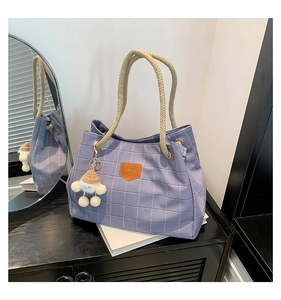 Detail of purple plaid tote bag with rope handles and a cute plush doll charm