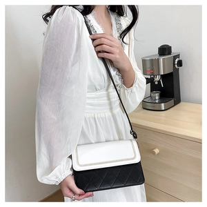 Detail of a black and white quilted crossbody bag worn by a model in a home setting