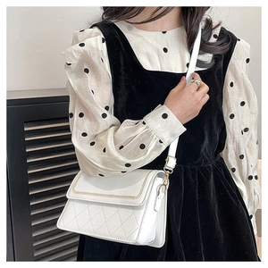 Detail of white quilted crossbody bag with gold chain trim and polished metal hardware