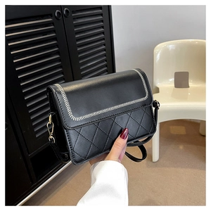 Detail of black quilted crossbody bag with fishbone stitching and metal hardware