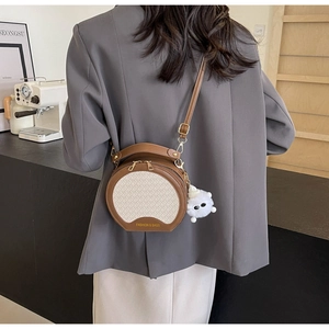 Detailansicht einer runden Patchwork-Handtasche mit Webstruktur und Plüsch-Anhänger am Model