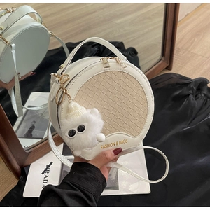 Detail der weißen runden Ledertasche mit gewebter Textur und flauschigem Monster-Anhänger