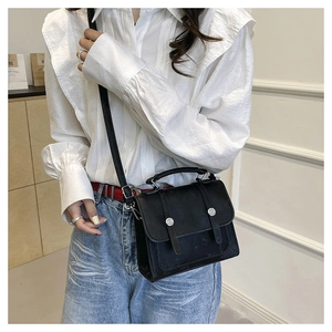 Detail of elegant black crossbody square bag with silver buckles and handle on model