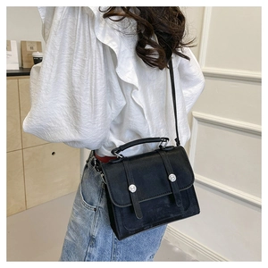Detail showing a black minimalist leather crossbody bag worn by a model in a casual setting