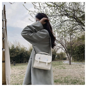 Detail view of a cream crossbody square bag with metal buckles on a grey suit jacket