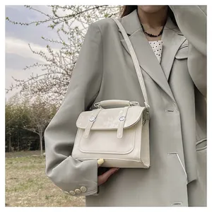 Elegant beige crossbody flap bag with silver buckle worn by a model in outdoor setting