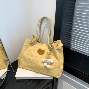 Yellow plaid tote bag with rope handles and cute fur ball charm on a dark desk
