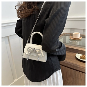 Detailed view of mini white crossbody bag with sparkling rhinestone bow and silver chain