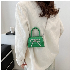Mini green sequin handbag with silver bow detail worn by a model in a white suit