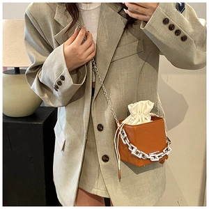 Close-up of brown textured small square bag with drawstring inner and silver chain strap