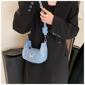 Close-up of light blue denim crescent bag with gold butterfly buckle and woven strap