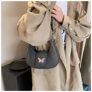 Detail of a grey half-moon underarm bag with a silver butterfly buckle worn with a trench coat
