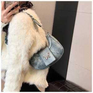 Detailed close-up of light blue denim hobo bag featuring a silver metal butterfly ornament