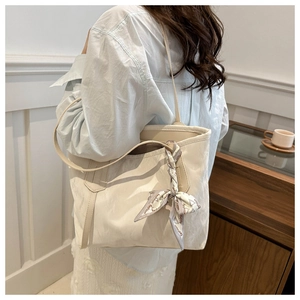 Detail of white tote bag featuring a decorative fashion scarf on the thin shoulder strap