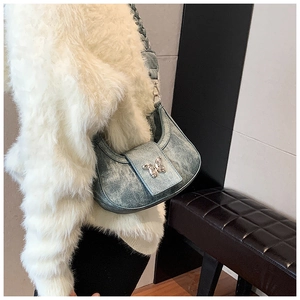 Detail of blue denim underarm bag featuring a sparkling silver butterfly and woven strap