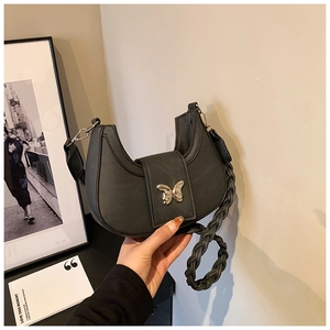 Detail of black half-moon bag featuring silver butterfly clasp and woven shoulder strap