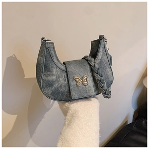 Detail of blue denim crescent bag featuring silver butterfly and braided strap