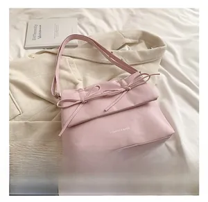 Detail of pink faux leather crossbody bag with dual bow accents and white fashion lettering