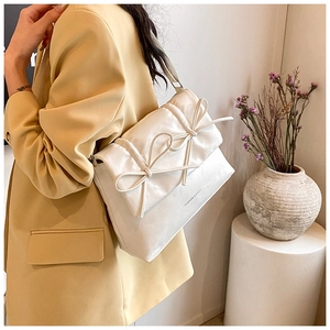 Detail of white quilted handbag with twin bows worn by model in a modern interior setting