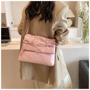 Close-up of pink bow shoulder bag with pleats and adjustable strap on a female model