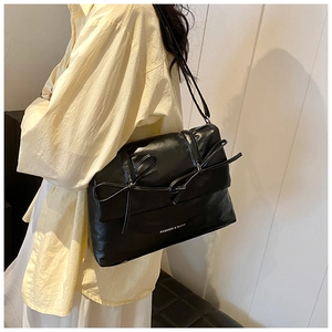 Detail of a black faux leather tote bag with dual bow accents and white lettering