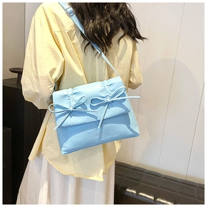 Close-up of light blue pleated shoulder bag featuring two bow knots and long strap